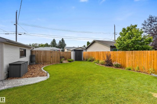 Fenced backyard featuring a manicured lawn, curved concrete edging, wood privacy fencing, and a detached exterior storage shed - 6207 85 Avenue Nw, Edmonton, AB 