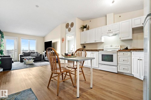 Wood-finish flooring throughout, white cabinetry with dark countertops, white range, vaulted ceiling, and patio door - #416 111 Edwards Dr Sw, Edmonton, AB 