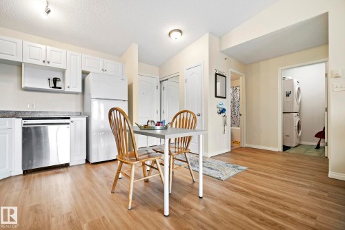 Kitchen featuring white cabinetry, stainless steel dishwasher, and wood-finish flooring - #416 111 Edwards Dr Sw, Edmonton, AB 
