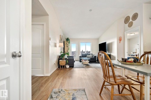 Open-concept living area with wood-finish flooring, vaulted ceilings, and a large glass door leading to an exterior balcony - #416 111 Edwards Dr Sw, Edmonton, AB 