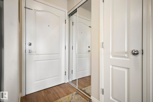 Wood-finish flooring with a mirrored closet door and white paneled doors - #416 111 Edwards Dr Sw, Edmonton, AB 