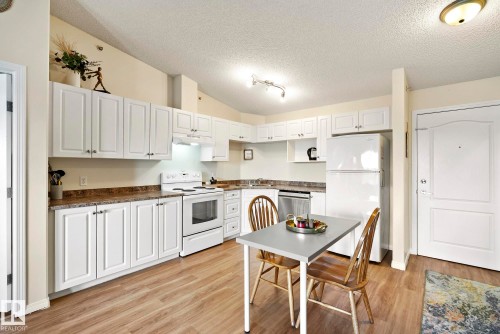 Kitchen featuring white cabinetry, wood-finish flooring, white appliances, and a built-in dishwasher - #416 111 Edwards Dr Sw, Edmonton, AB 