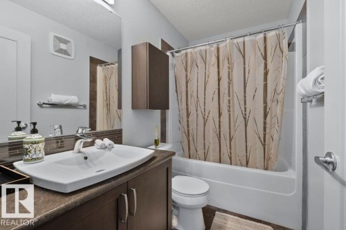 Bathroom featuring a vanity with dark wood-finish cabinetry, a stone-composite countertop, an integrated porcelain sink, and a large wall-mounted mirror - 6818 Evans Wynd Nw, Edmonton, AB 