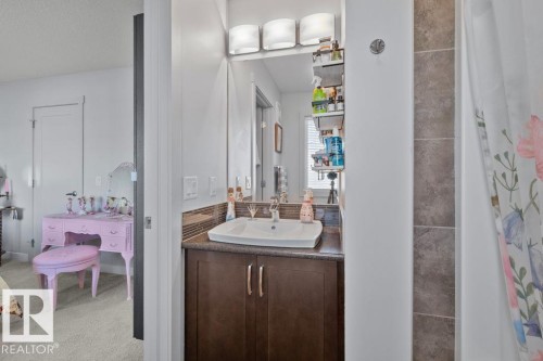 Bathroom vanity featuring a dark wood-finish cabinet, rectangular vessel sink, stone-finish countertop, three-light frosted glass fixture, and horizontal tile backsplash - 6818 Evans Wynd Nw, Edmonton, AB 
