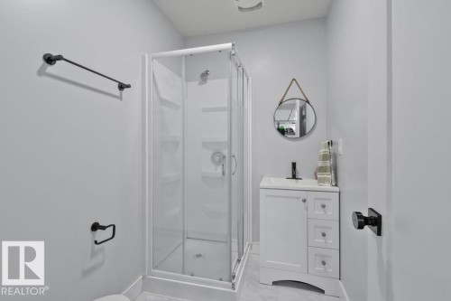 Enclosed shower with glass sliding doors, vanity featuring integrated sink, matte black hardware, and neutral stone-finish flooring - 6818 Evans Wynd Nw, Edmonton, AB 