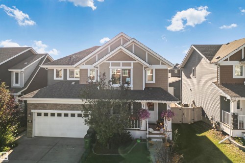 Multi-level exterior featuring horizontal and shake siding, a front porch with white railing, stone veneer accents, and an attached two-car garage - 6818 Evans Wynd Nw, Edmonton, AB 