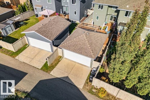 Detached garage featuring a hip roof, white overhead door, concrete apron, and wood-style privacy fencing - 6818 Evans Wynd Nw, Edmonton, AB 