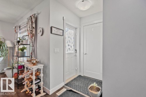 Entryway featuring wood-finish flooring, a white paneled door with patterned glass insert, and a flush-mount ceiling light - 6818 Evans Wynd Nw, Edmonton, AB 