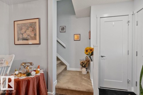 Interior entryway featuring a staircase with carpeted treads, a solid-core single-panel door with brushed nickel hardware, and neutral wall tones - 6818 Evans Wynd Nw, Edmonton, AB 