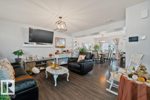 Open-concept living space featuring wood-finish flooring, a wall-mounted fireplace mantel, and geometric lantern-style lighting - 6818 Evans Wynd Nw, Edmonton, AB 