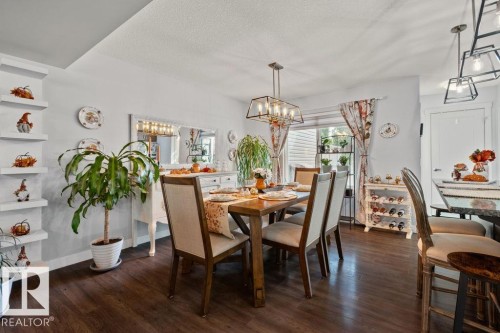 Dining area featuring dark wood-finish flooring, built-in recessed shelving, a geometric metal chandelier, and a breakfast bar - 6818 Evans Wynd Nw, Edmonton, AB 