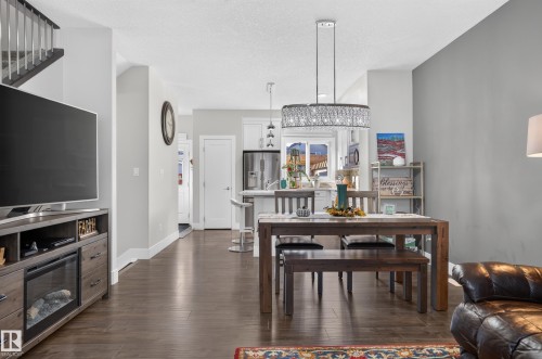 Open-concept interior featuring wood-finish flooring, a tiered drum pendant light with crystal accents, white cabinetry, and a kitchen island - 798 Berg Loop, Leduc, AB 