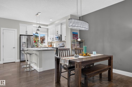 Kitchen featuring white cabinetry, an island with stone-composite countertop, wood-finish flooring, and a crystal-accented linear pendant light fixture - 798 Berg Loop, Leduc, AB 