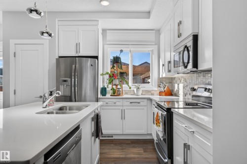 Kitchen featuring white shaker cabinetry, quartz countertops, a mosaic tile backsplash, stainless steel appliances, and wood-finish flooring - 798 Berg Loop, Leduc, AB 