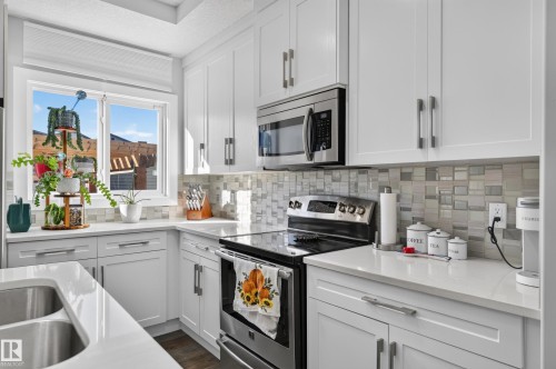 Kitchen featuring white shaker-style cabinetry, stainless steel appliances, quartz countertops, a multi-tonal glass tile backsplash, and an undermount double-basin sink - 798 Berg Loop, Leduc, AB 