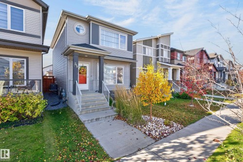 Two-story home featuring horizontal siding, a circular accent window, a covered front porch with stone foundation pillars, and concrete stairs with metal railings - 798 Berg Loop, Leduc, AB 