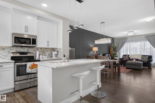 Kitchen featuring white cabinetry, stone-finish countertops, stainless steel appliances, multi-toned tile backsplash, and wood-finish flooring - 798 Berg Loop, Leduc, AB 