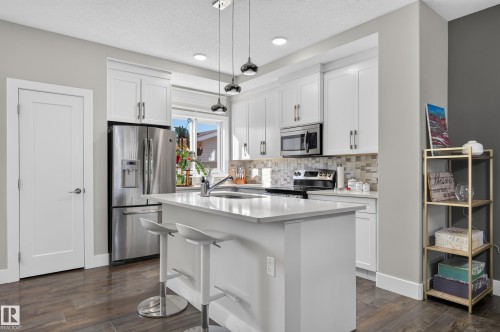 Kitchen featuring white cabinetry, quartz countertops, a central island with a stainless steel sink, tile backsplash, and stainless steel appliances - 798 Berg Loop, Leduc, AB 