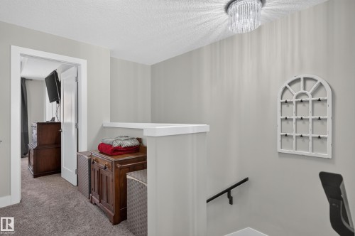 Neutral-toned interior space featuring a multi-tiered crystal flush-mount light fixture, a low-profile wall partition with white trim, and a black metal handrail - 798 Berg Loop, Leduc, AB 