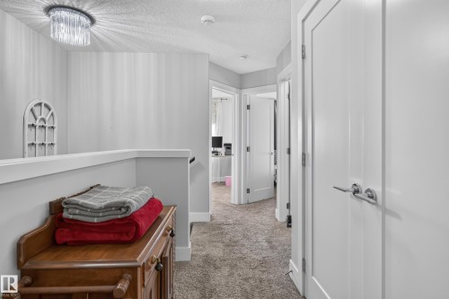 Hallway featuring wall-to-wall carpeting, three-panel interior doors with brushed nickel lever handles, and a decorative crystal flush-mount ceiling fixture - 798 Berg Loop, Leduc, AB 