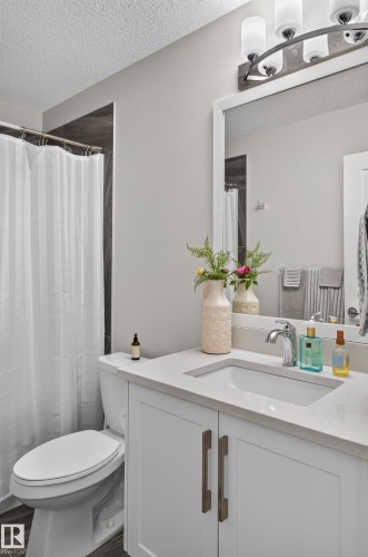 White vanity with a neutral solid-surface countertop, rectangular undermount sink, brushed metal hardware, and a multi-bulb light fixture above a framed mirror - 798 Berg Loop, Leduc, AB 