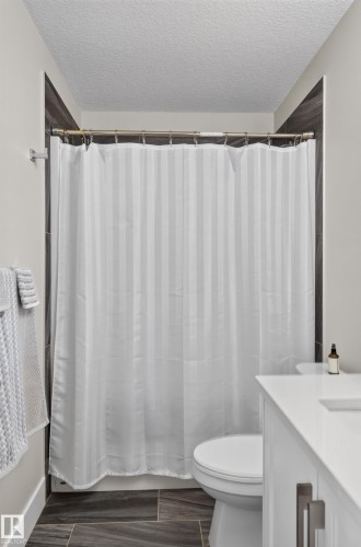Shower alcove featuring large-format dark tile surround, integrated white vanity with solid-surface countertop, and dark-toned tile flooring - 798 Berg Loop, Leduc, AB 