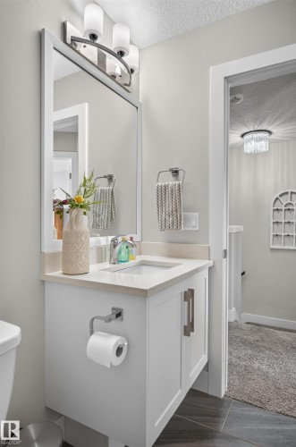 White vanity featuring a solid surface countertop, integrated rectangular basin, brushed nickel hardware, and a three-light wall-mounted fixture with a matching framed mirror - 798 Berg Loop, Leduc, AB 