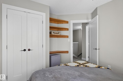 Dual-door closet featuring matte black hardware, custom built-in wood-finish corner shelving, and neutral wall tones - 798 Berg Loop, Leduc, AB 