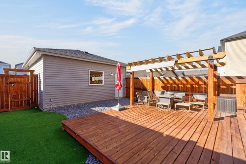 Backyard featuring a wood deck, integrated timber pergola, artificial turf lawn, decorative stone perimeter, and wood privacy fencing - 798 Berg Loop, Leduc, AB 