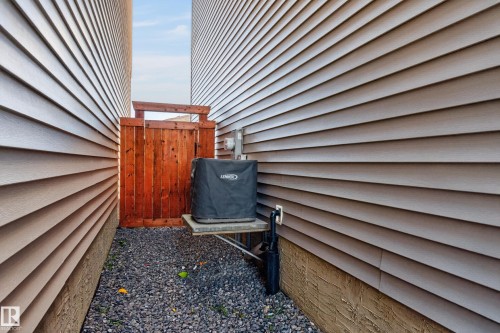 Side exterior featuring light-colored horizontal siding, stone foundation trim, gravel ground cover, and a wood privacy gate - 798 Berg Loop, Leduc, AB 