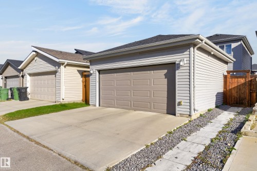 Detached garage featuring horizontal siding, a paneled overhead door, a concrete driveway, and an attached wood privacy gate - 798 Berg Loop, Leduc, AB 