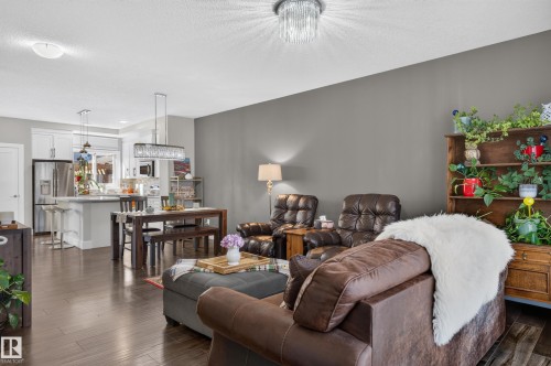 Open-concept interior featuring wood-finish flooring, white cabinetry, a kitchen island, and tiered crystal-style light fixtures - 798 Berg Loop, Leduc, AB 