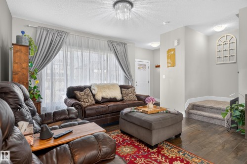 Living area featuring wood-finish flooring, a decorative crystal flush-mount light fixture, and carpeted stairs with a tiered elevation - 798 Berg Loop, Leduc, AB 