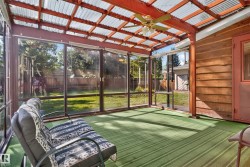 Screened sunroom featuring a corrugated translucent roof, wood beam construction, ceiling fan, and green striped flooring - 