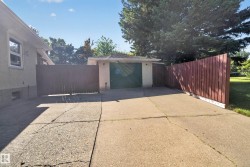 Detached garage with a dark green overhead door, concrete driveway, and wood-panel fencing - 