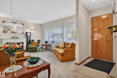 Living area featuring a fireplace with a white mantel, light-colored carpeting, and a wood-finish entry door - 14 Sonora Drive, St. Albert, AB 