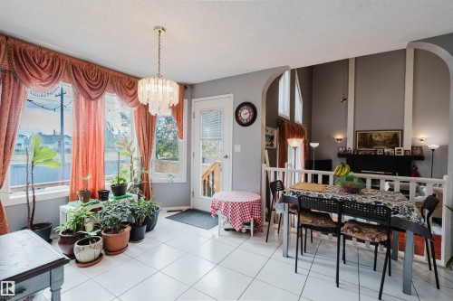 Multi-level living area featuring white tile flooring, vaulted ceilings, a prominent fireplace with a dark mantle, and a tiered architectural design with an arched divider and white railing - 225 Heagle Crescent Nw, Edmonton, AB 