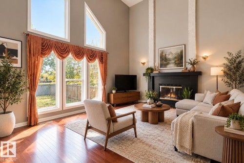 Vaulted ceilings featuring expansive windows, wood-finish flooring, and a floor-to-ceiling fireplace with a dark surround and dual decorative columns - 225 Heagle Crescent Nw, Edmonton, AB 