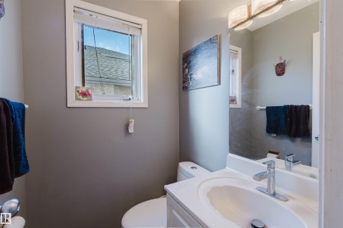 Bathroom featuring a white vanity cabinet with an integrated sink, a chrome single-handle faucet, a large wall-mounted mirror, and a multi-light fixture - 225 Heagle Crescent Nw, Edmonton, AB 