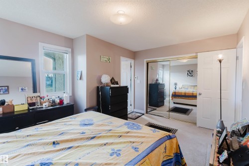 Bedroom featuring wall-to-wall carpeting, dual-pane window with white trim, and a sliding mirrored closet door with gold-tone framing - 225 Heagle Crescent Nw, Edmonton, AB 