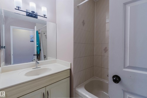 Bathroom vanity featuring a solid-surface countertop with an integrated basin, three-light fixture, expansive wall-mounted mirror, and tile-surround bathtub - 225 Heagle Crescent Nw, Edmonton, AB 