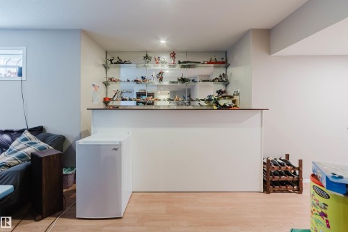 Built-in wet bar featuring a solid-surface countertop, mirrored back panel, and tiered glass shelving - 225 Heagle Crescent Nw, Edmonton, AB 