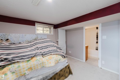 Room with carpeted flooring, window with security bars, and doorway entry to a bathroom featuring a tub-shower combination and vanity - 225 Heagle Crescent Nw, Edmonton, AB 