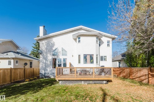 Rear exterior featuring a raised wood deck with lattice skirting, custom architectural windows, a stucco facade, an exterior chimney, and a full-perimeter wood privacy fence - 225 Heagle Crescent Nw, Edmonton, AB 