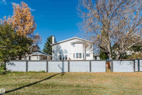 Exterior featuring a light-colored stucco facade, vertical and triangular windows, an integrated chimney, and a full-perimeter privacy fence - 225 Heagle Crescent Nw, Edmonton, AB 