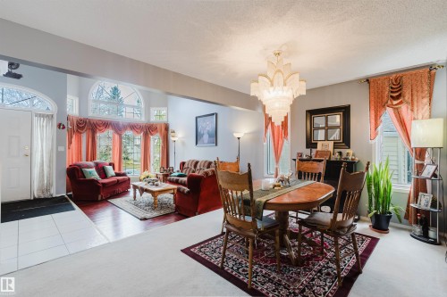 Open-concept interior featuring wood-finish flooring, multi-pane arched windows, tile entry flooring, and a tiered crystal chandelier - 225 Heagle Crescent Nw, Edmonton, AB 