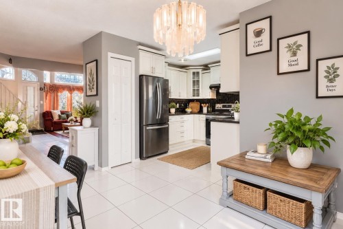 Kitchen featuring white cabinetry, dark countertops, black tile backsplash, stainless steel appliances, and a glass-accented chandelier - 225 Heagle Crescent Nw, Edmonton, AB 
