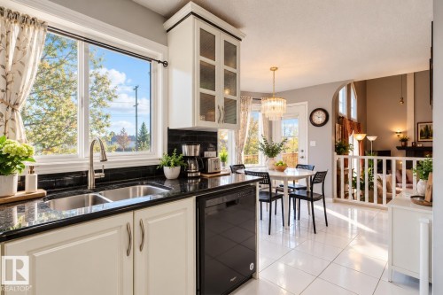 Kitchen featuring white cabinetry with glass-front uppers, dark stone countertops, a subway tile backsplash, dual-basin undermount sink, and polished tile flooring - 225 Heagle Crescent Nw, Edmonton, AB 