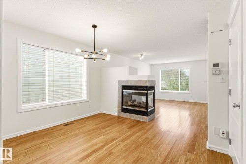 Wood-finish flooring throughout, featuring a modern chandelier, large windows with blinds, and a built-in fireplace with a tiled surround - 2550 Rabbit Hill Road Nw, Edmonton, AB 