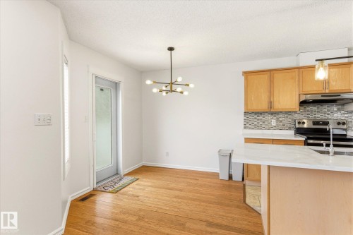 Wood-finish flooring, contemporary ceiling light fixture, kitchen with wood cabinetry, tile backsplash, and a countertop island - 2550 Rabbit Hill Road Nw, Edmonton, AB 